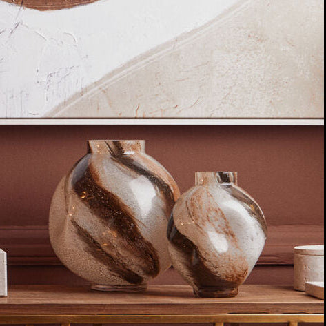 Decorative setup with vases, a mirror, and abstract wall art on a brown wall.