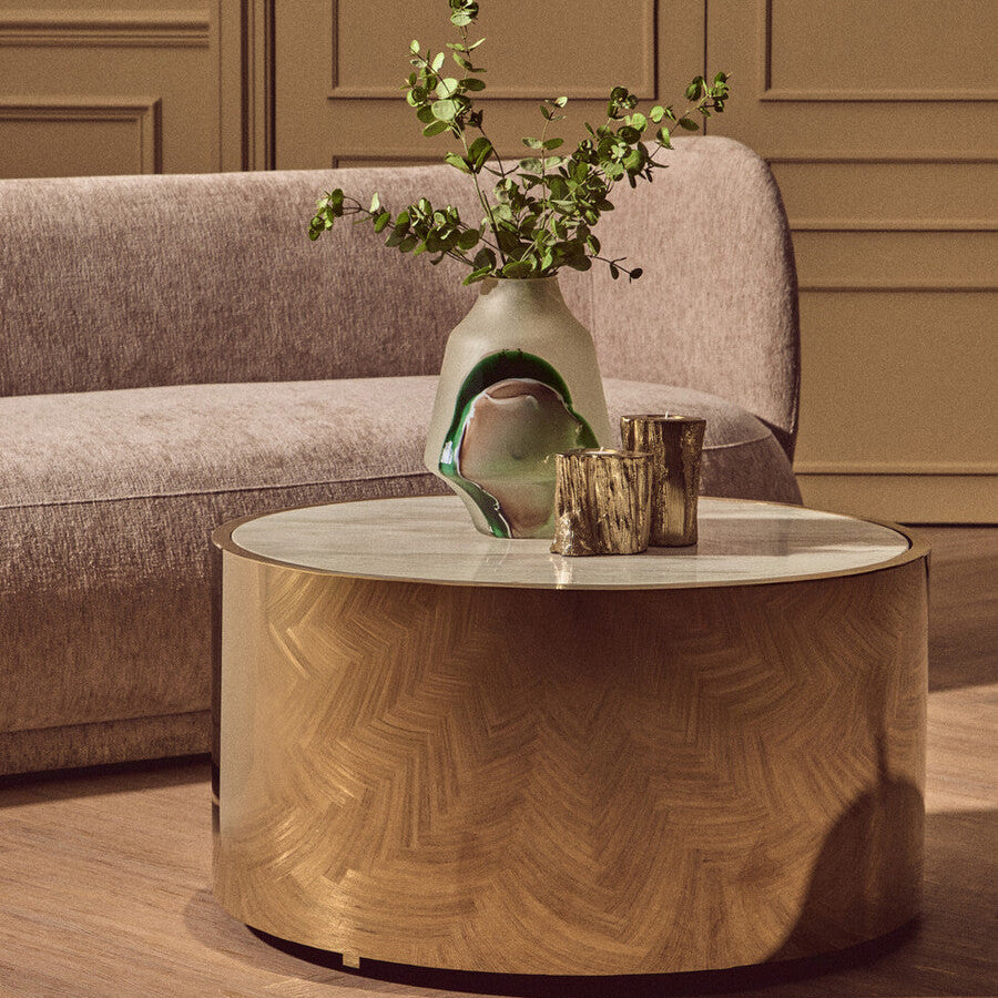 Round wooden coffee table with a vase and glasses in a living room setting.