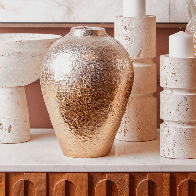 Decorative vases and candles on a surface with a marble wall background
