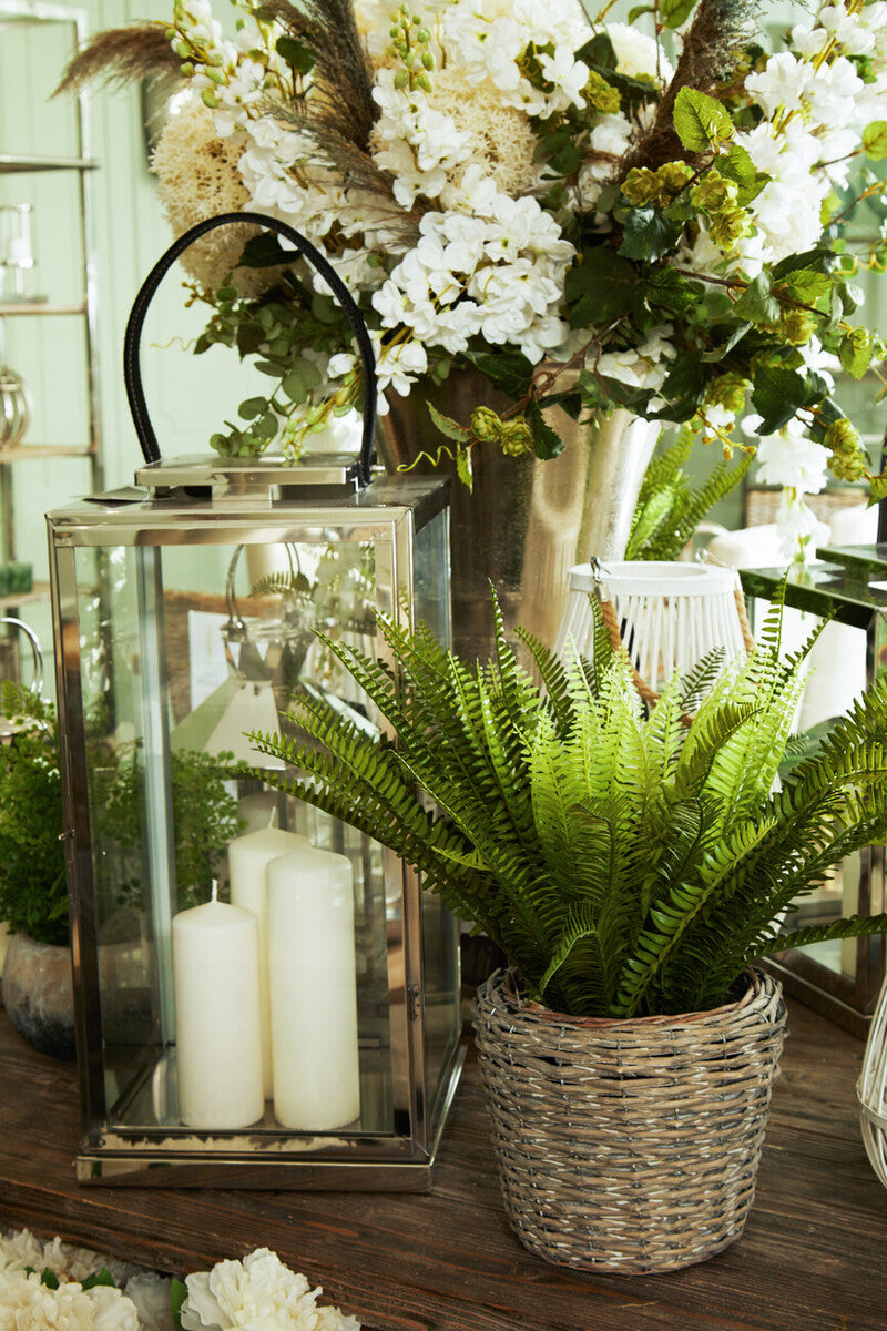 Decorative setup with a lantern, candles, and potted plants on a wooden surface.