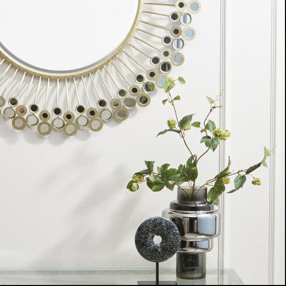 Decorative round mirror with a unique frame design on a white wall.