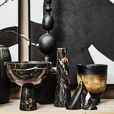 Collection of black and brown ceramic vases on a wooden surface with abstract art in the background.