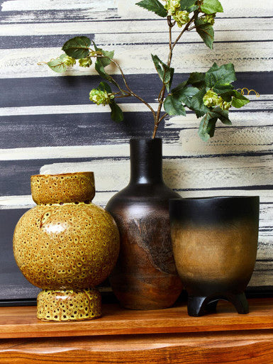 Three decorative vases on a wooden surface with a striped wall in the background