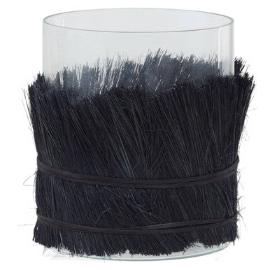 Clear glass candle holder with black decorative straw-like material wrapped around it on a white background