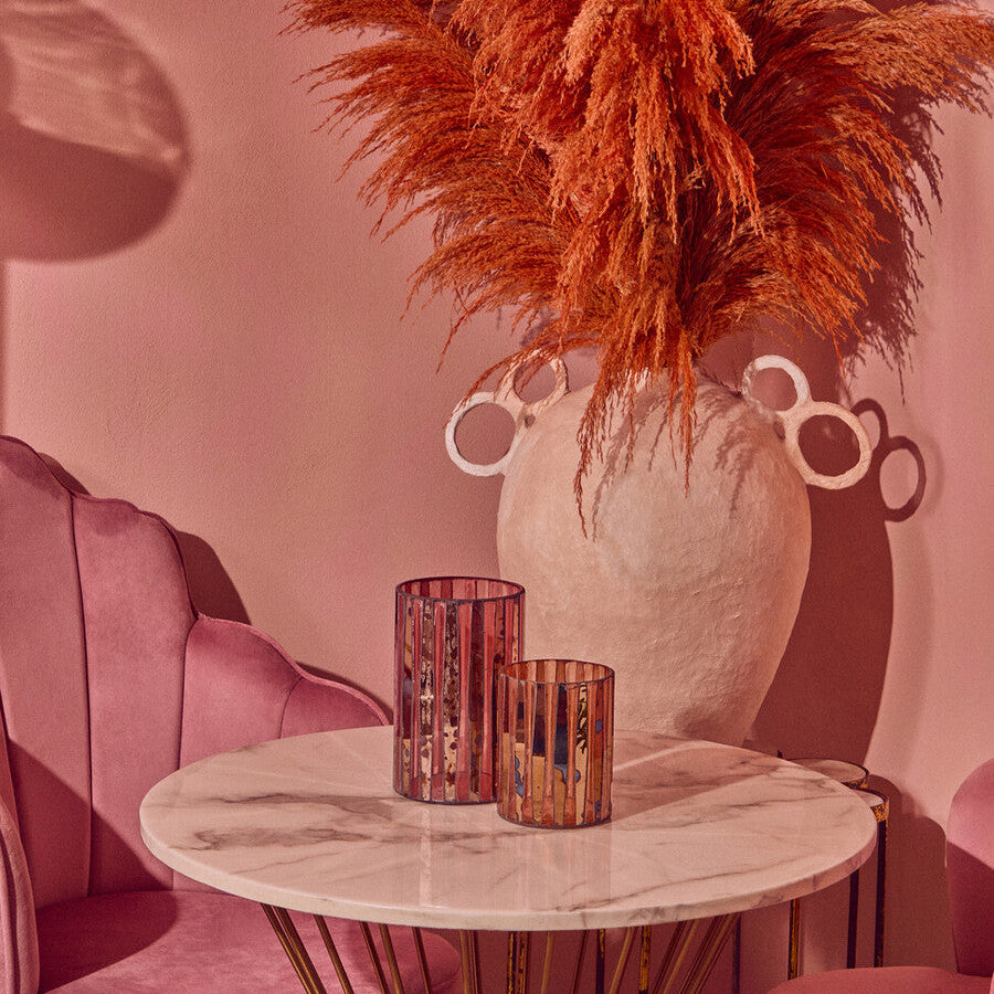 Decorative vase with orange pampas grass on a marble table against a pink wall.