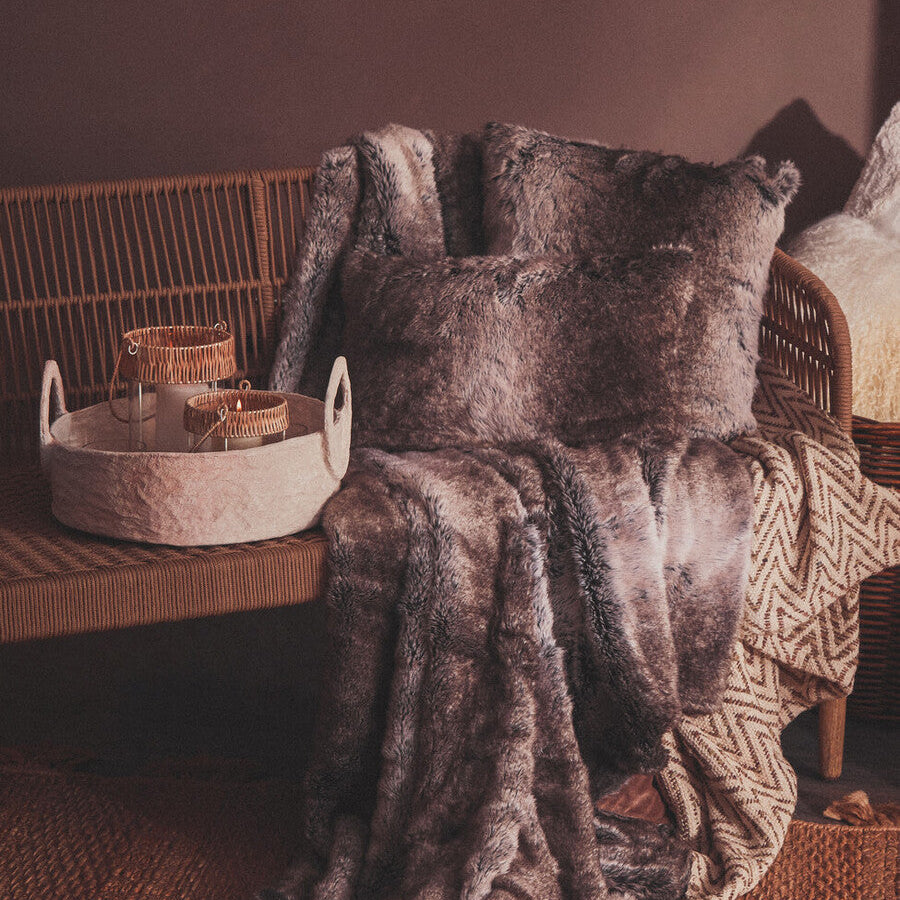 Brown textured blanket draped over a wicker chair with a basket on a wooden surface.