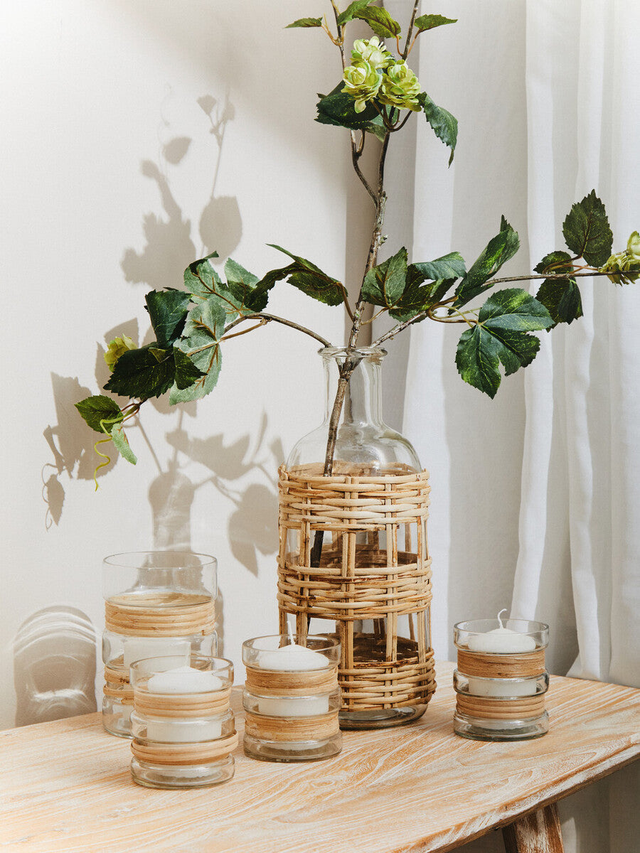 Decorative setting with glass vases, candles, and a woven vase on a wooden surface.