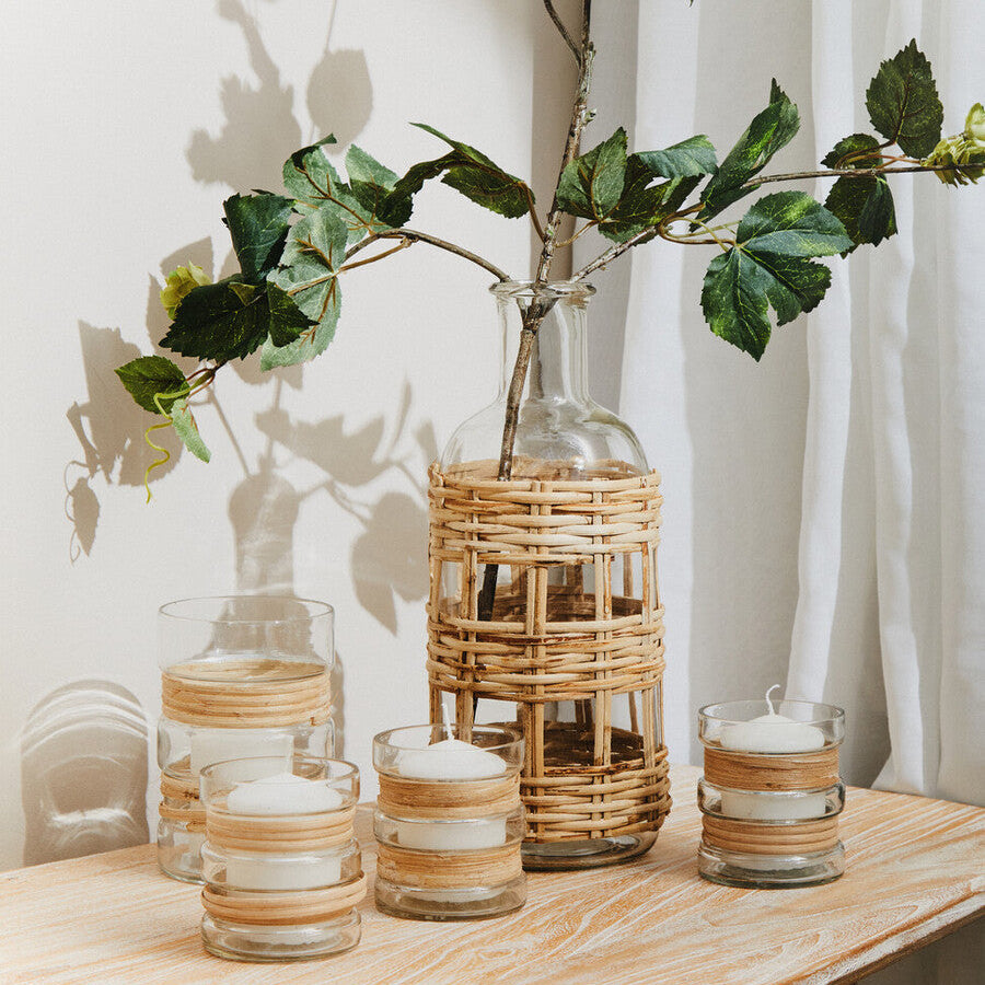 Decorative setting with glass vases, candles, and a woven vase on a wooden surface.