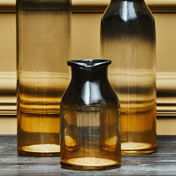 Three gradient glass vases on a wooden surface with a gold wall background