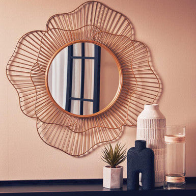 Decorative wall mirror with wicker-like frame on a beige wall above a dark surface with decorative items.