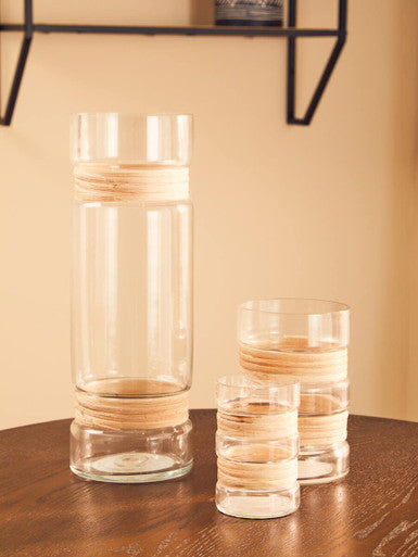Two glass vases with wooden accents on a wooden surface against a beige wall.