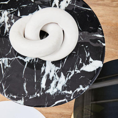 White ceramic donut-shaped object on a black marble-patterned stand.