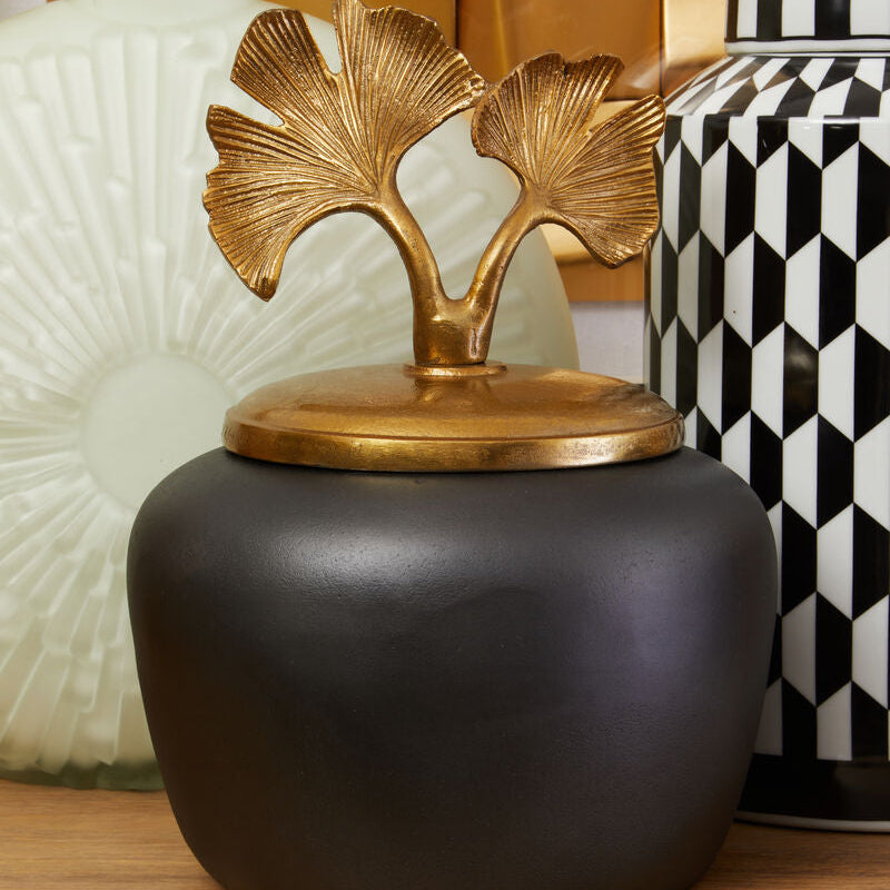 Decorative black jar with gold leaf design on a wooden surface