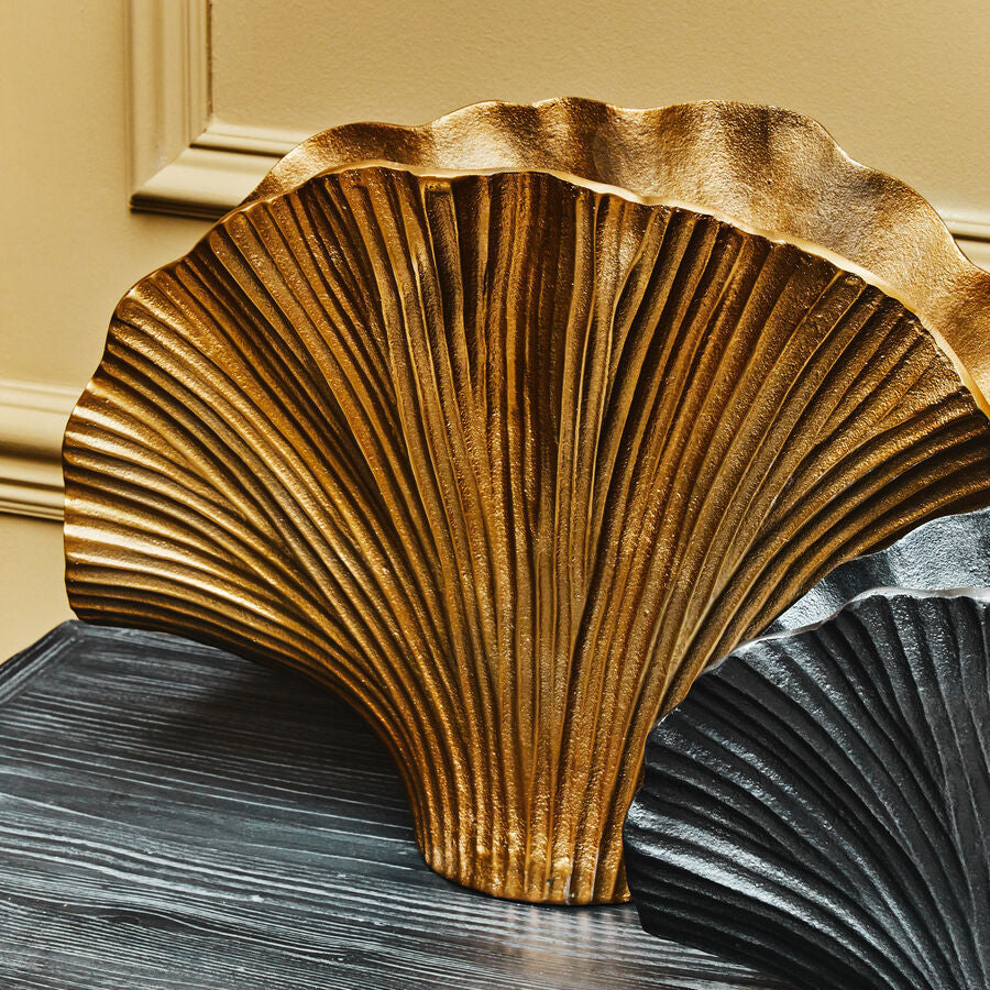 Decorative gold shell sculpture on a dark surface with a beige wall background