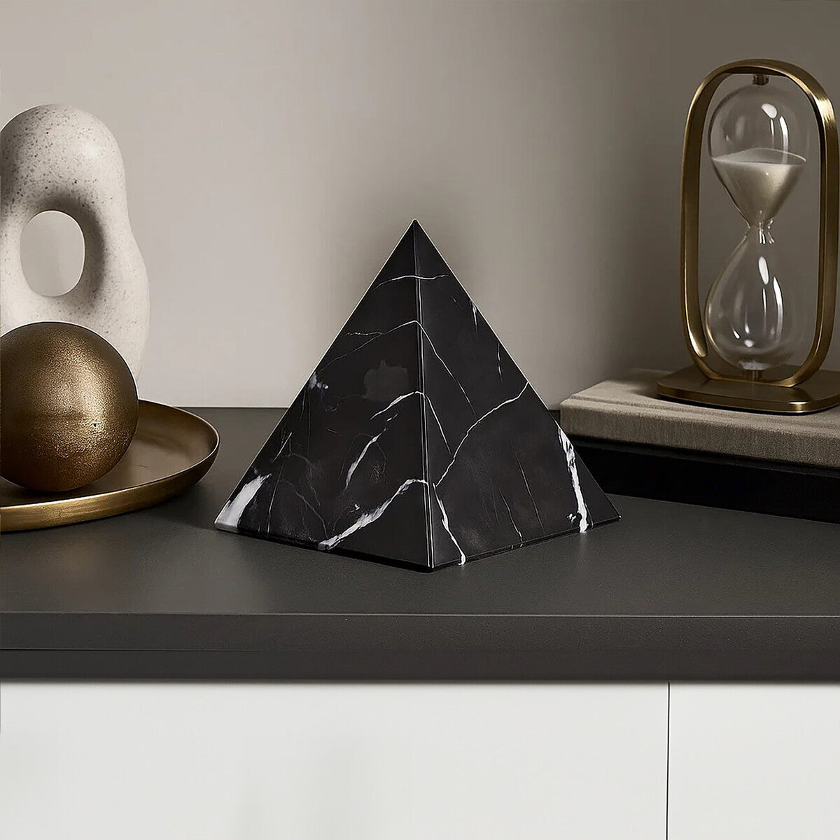 Black marble pyramid on a dark surface with decorative items in the background