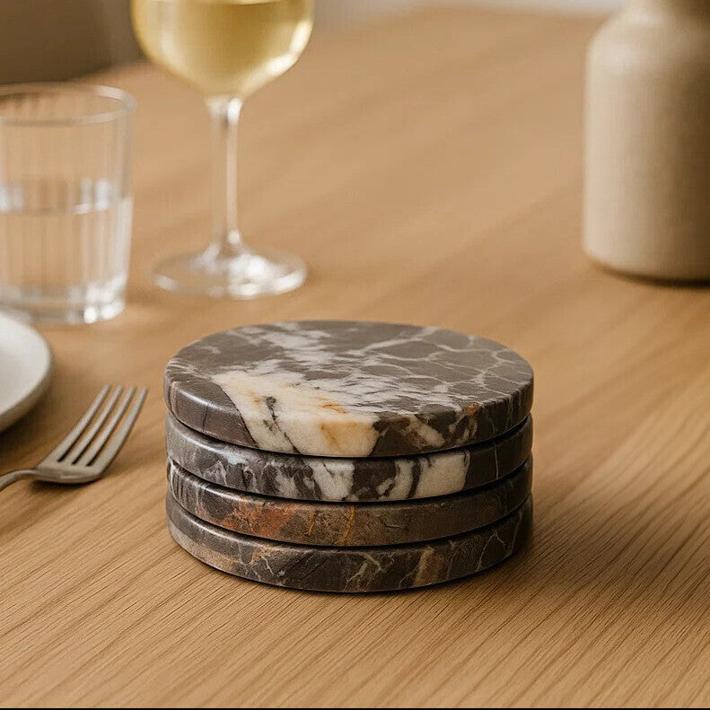 Stack of marble coasters on a wooden table with a glass of wine and a vase in the background.