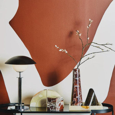 Modern interior design with a glass table, vase, and lamp against a abstract wall.