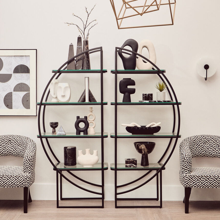 Modern interior with a black circular shelving unit, decorative items, and patterned armchairs.