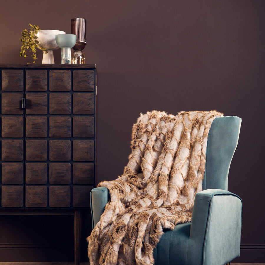 Blue armchair with a fur throw blanket in a room with a dark brown wall and wooden floor.