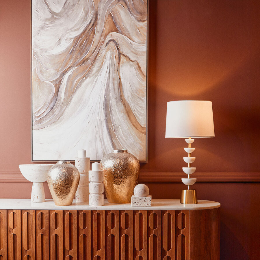 Decorative interior setting with a wooden console table, lamp, and abstract painting on a pink wall.
