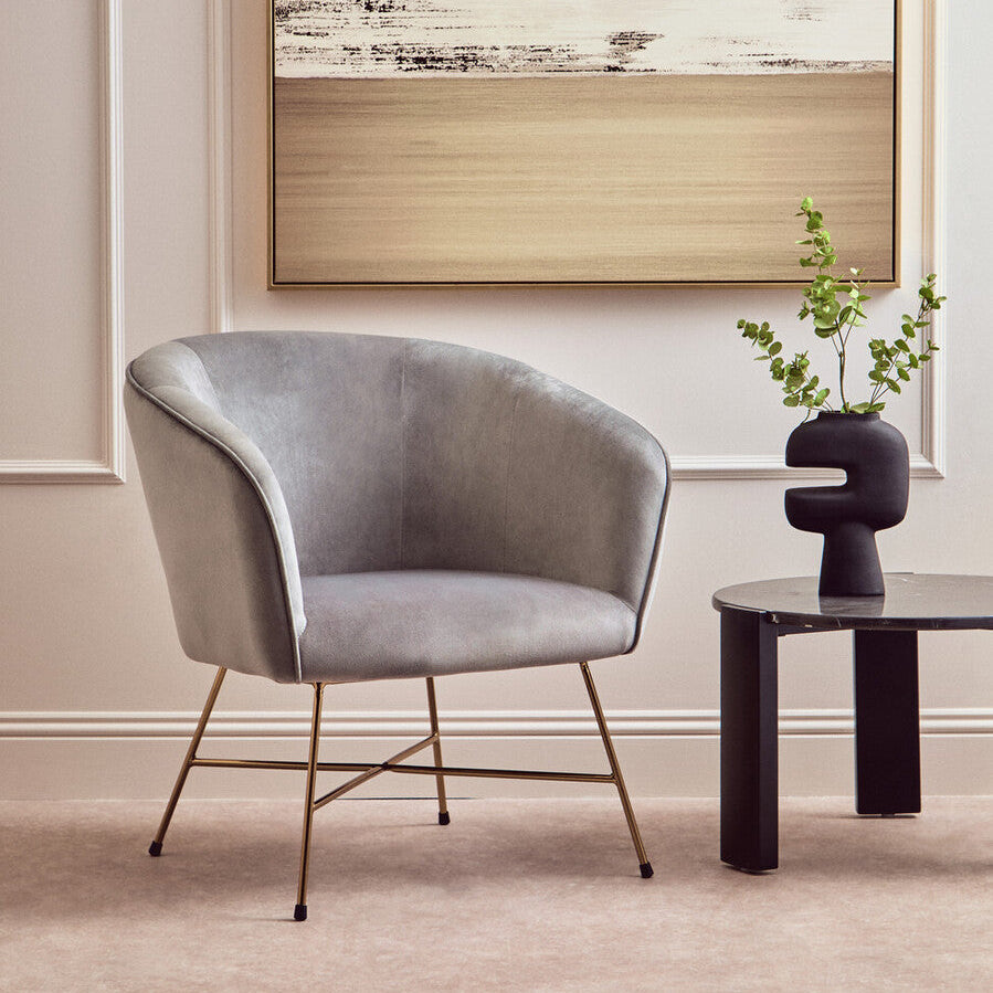 Gray armchair in a room with abstract art on the wall and a small table with a plant.