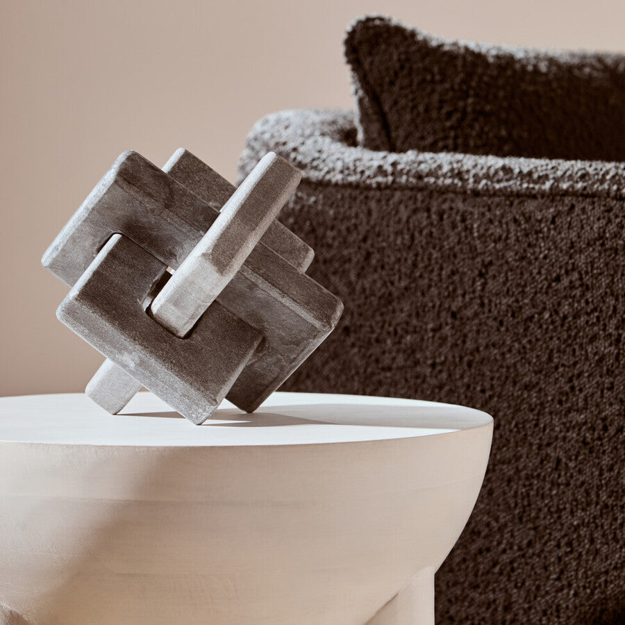 Decorative stone sculpture on a white pedestal with a textured brown sofa in the background