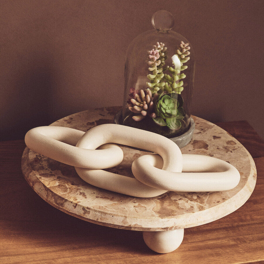 Decorative ceramic chain on a wooden surface with a glass dome containing plants.
