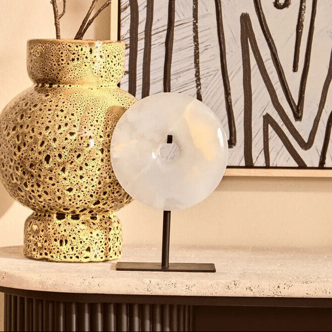 Decorative table with gold vase, white lamp, and abstract art in the background