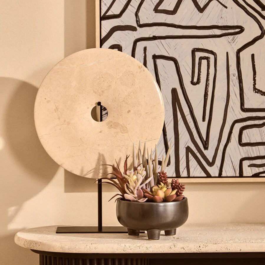 Decorative table with a round stone sculpture, small plant pot, and abstract wall art.