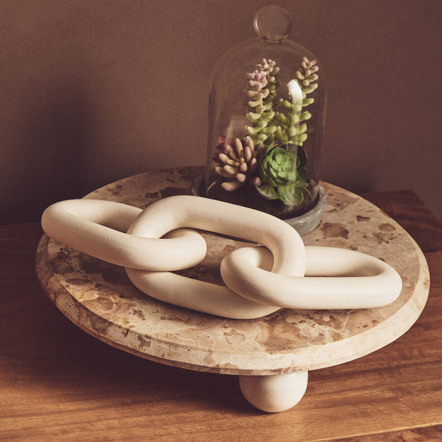 Decorative ceramic chain on a wooden surface with a glass dome containing plants.