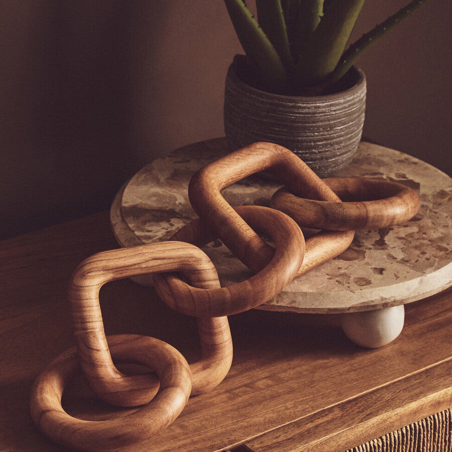 Wooden chain sculpture on a stone surface with a potted plant in the background