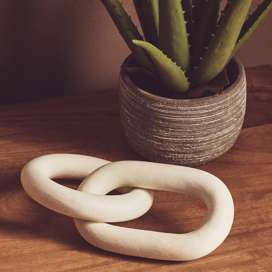 Decorative white ceramic knot on a wooden surface with a potted plant in the background