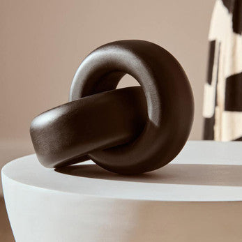 Wooden knot sculpture on a white pedestal against a neutral background