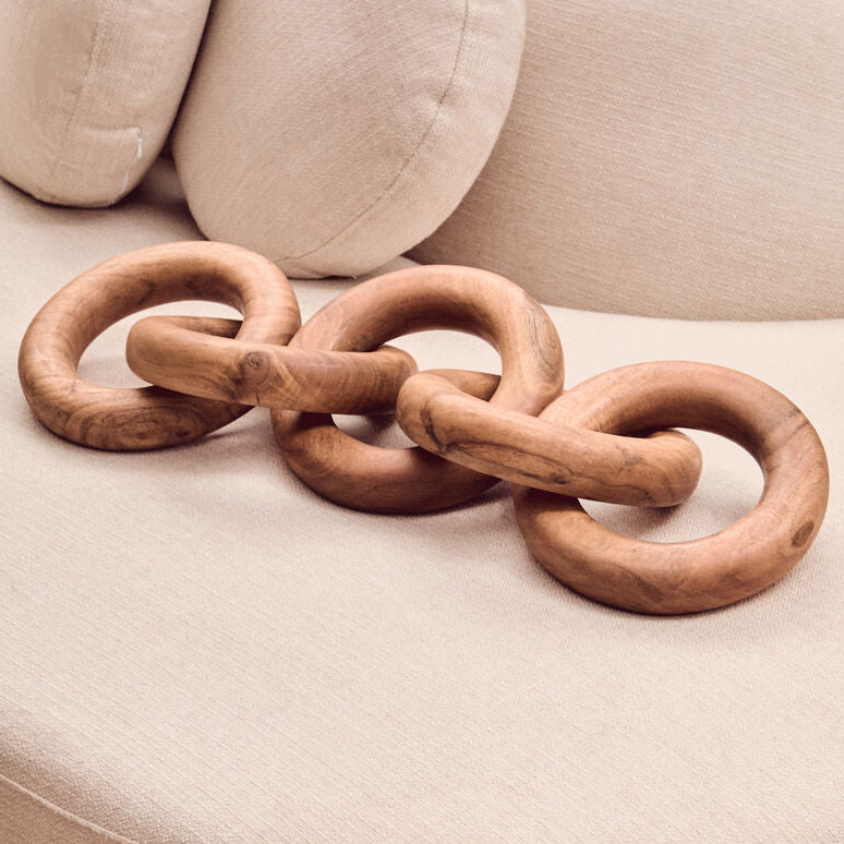 Wooden chain-like decorative item on a beige cushioned surface