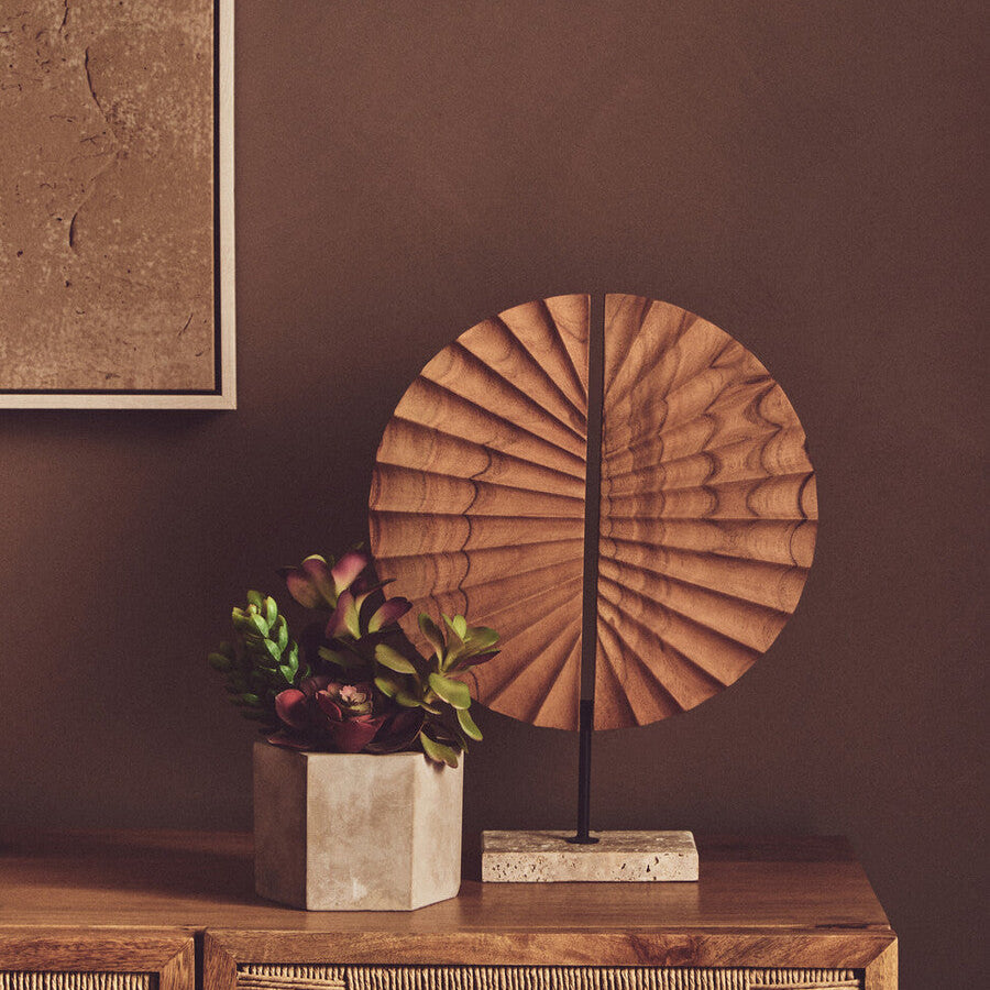 Decorative wooden sculpture and plant on a wooden surface with a brown wall background