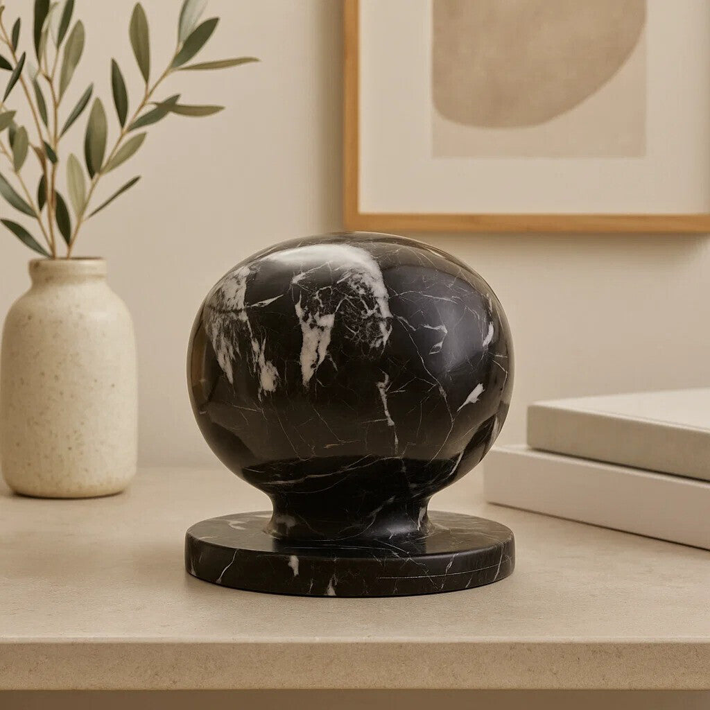 Black marble sphere on a beige surface with a vase and plant in the background