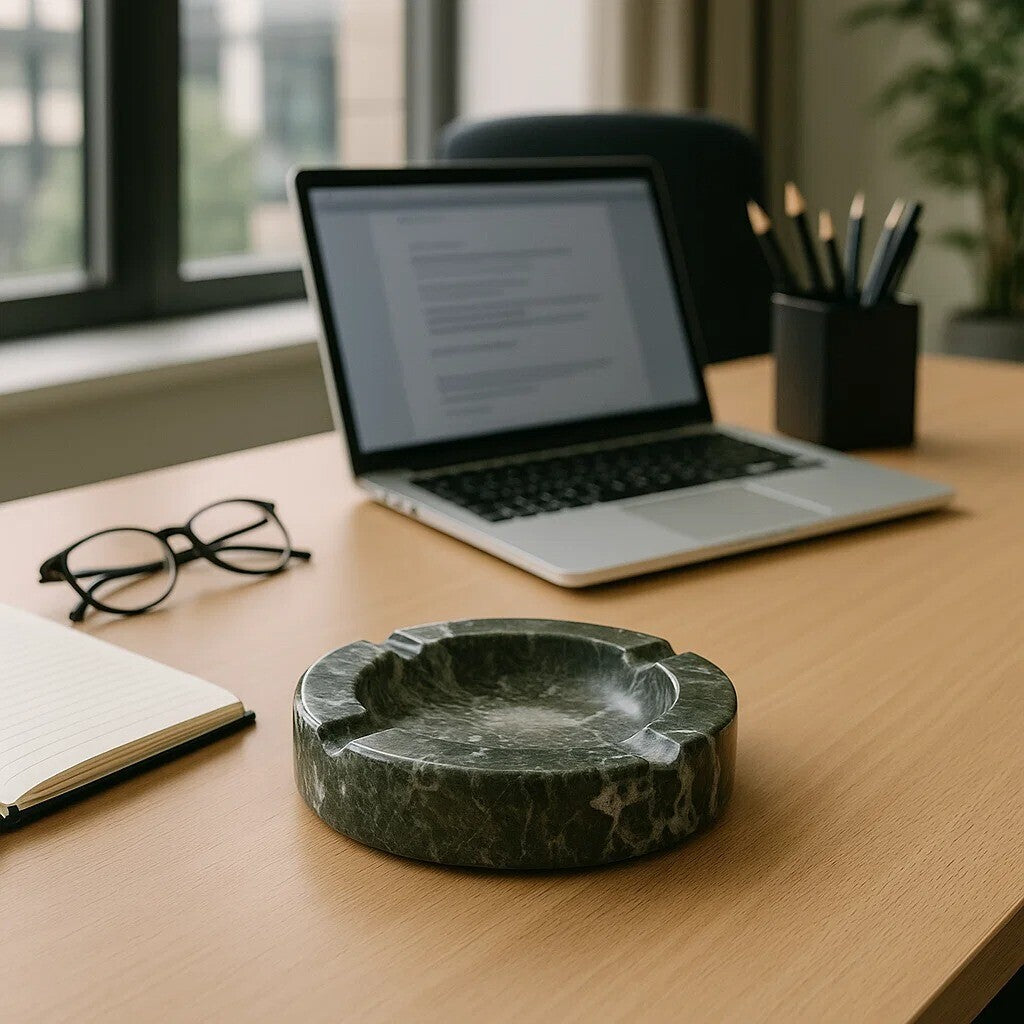 Marble ashtray on a desk with a laptop, glasses, and notebook in the background.