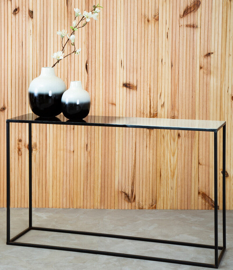 Black console table with two black and white vases against a wooden wall.