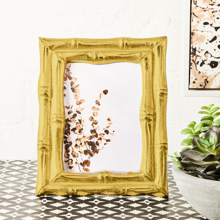 Gold picture frame on a table with a white wall and plant in the background