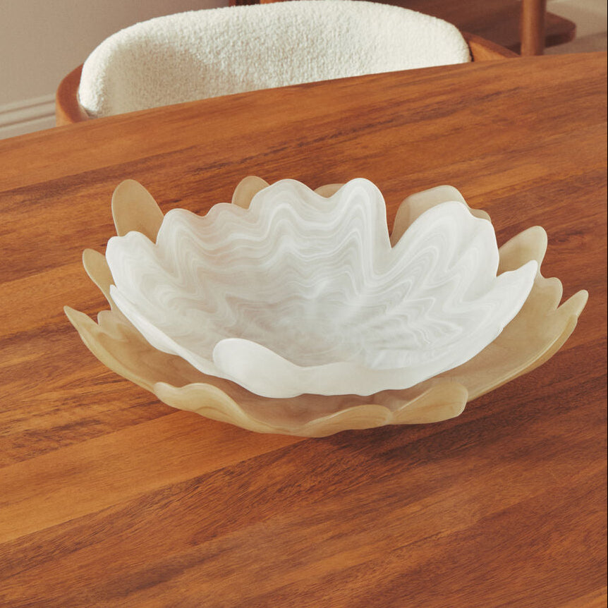 Decorative white shell-shaped bowl on a wooden surface with a wooden shelf in the background.