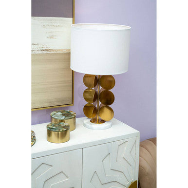 Decorative lamp with gold base on a white cabinet against a purple wall