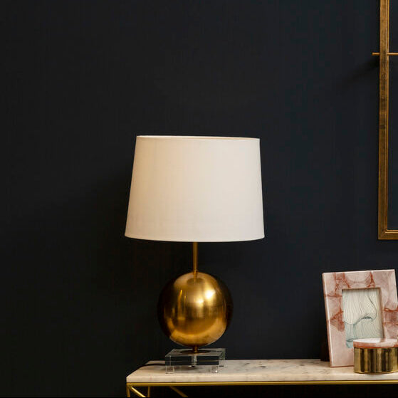 Gold wall clock on a dark wall with a lamp and decorative items on a table.