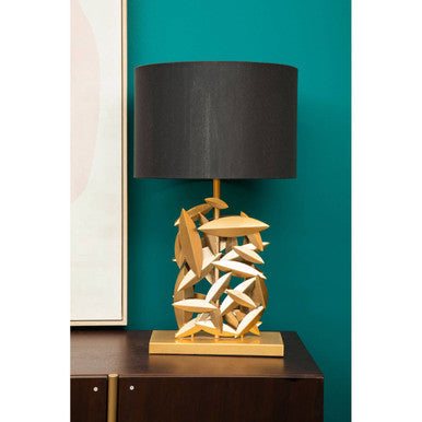 Decorative table lamp with gold base and black shade against a teal wall.