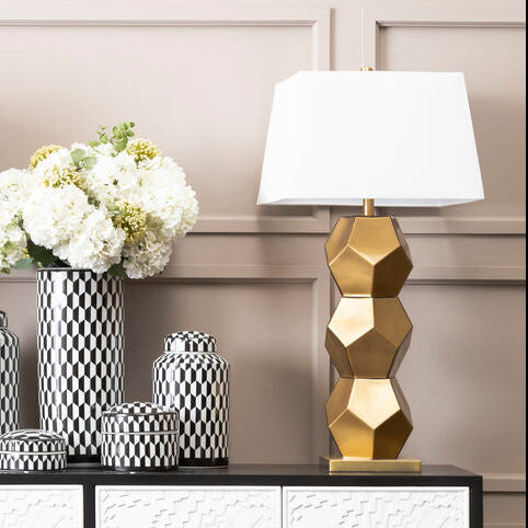 Decorative console table with lamps, vases, and a flower arrangement against a paneled wall.