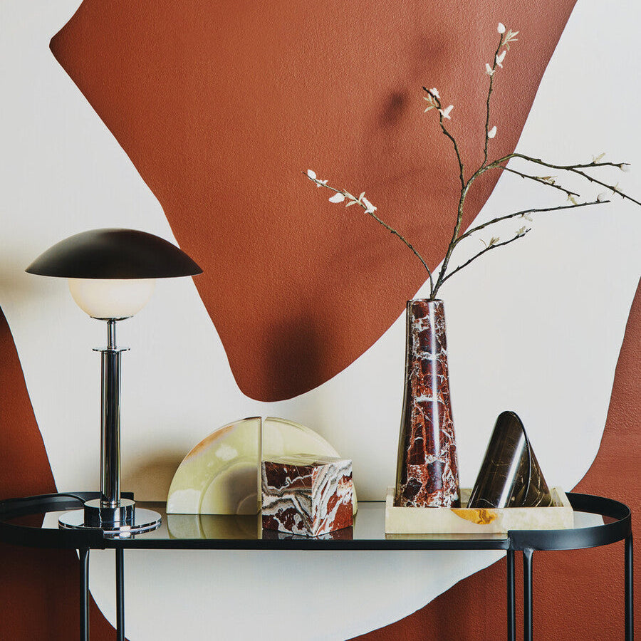 Modern interior design with a glass table, lamp, and decorative items against a wall with abstract brown and white shapes.