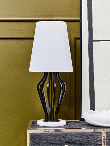 Table lamp with a white shade on a wooden surface against a green wall.