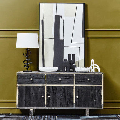 Black wooden sideboard with abstract art and lamp against a green wall