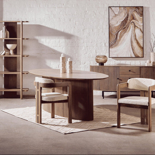 Dining room with wooden table and chairs, bookshelf, and abstract painting on a white brick wall.