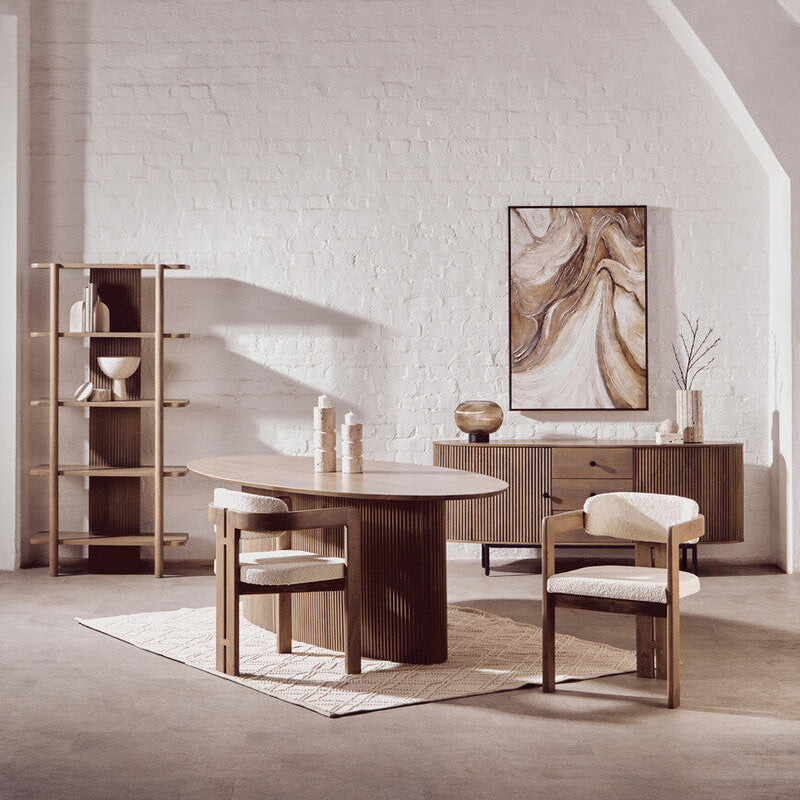 Dining room with wooden table and chairs, bookshelf, and abstract painting on a white brick wall.