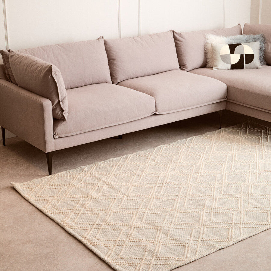 Beige sectional sofa with decorative pillows on a patterned rug in a living room.